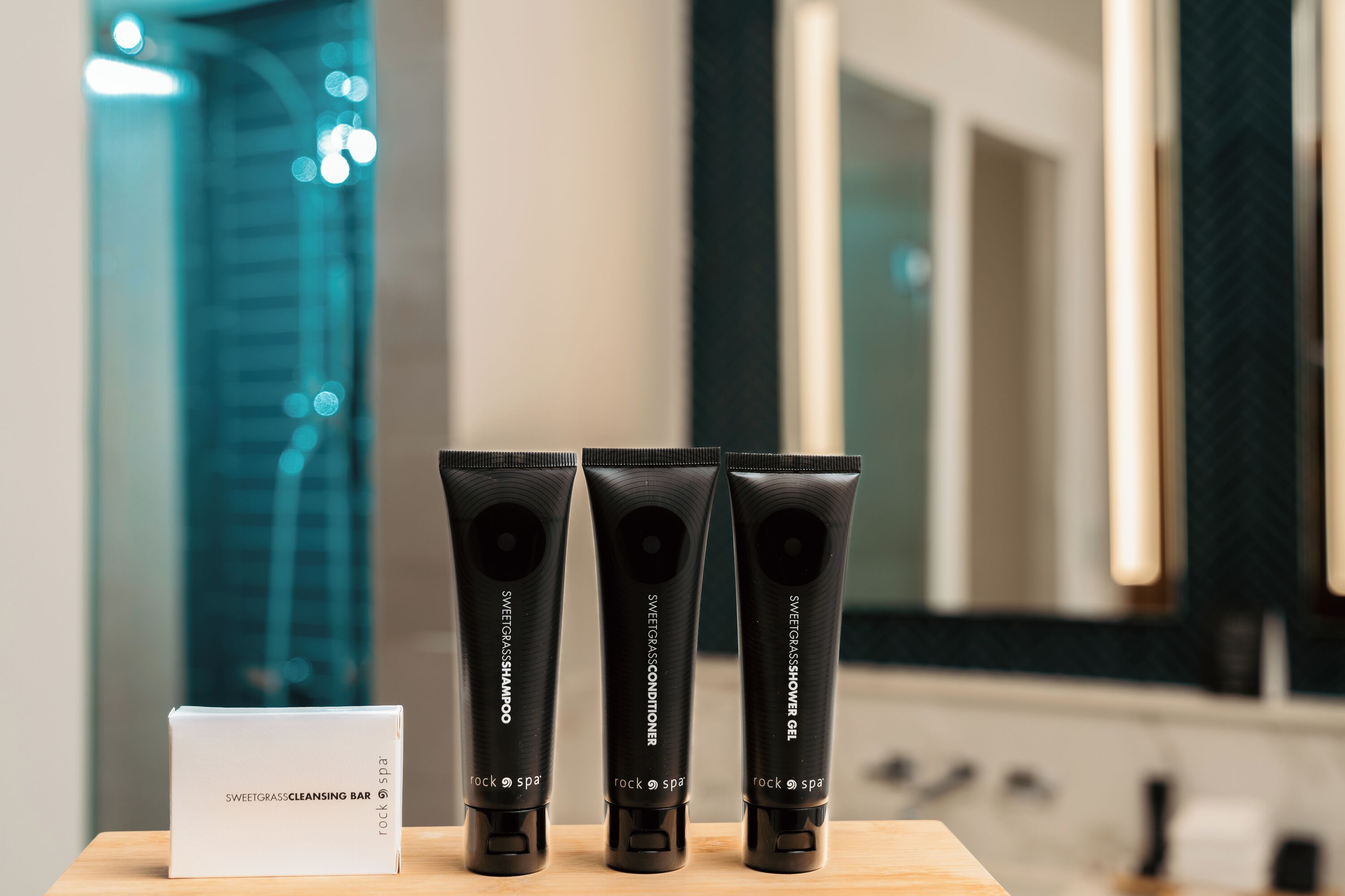 Three black tubes of Sweetgrass products on a wooden surface with a white box labeled 'Sweetgrass Cleansing Bar' and a mirror in the background.