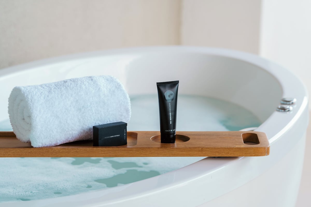 Eine Badewanne mit einem Holztablett, das ein weißes Handtuch und eine schwarze Flasche trägt.