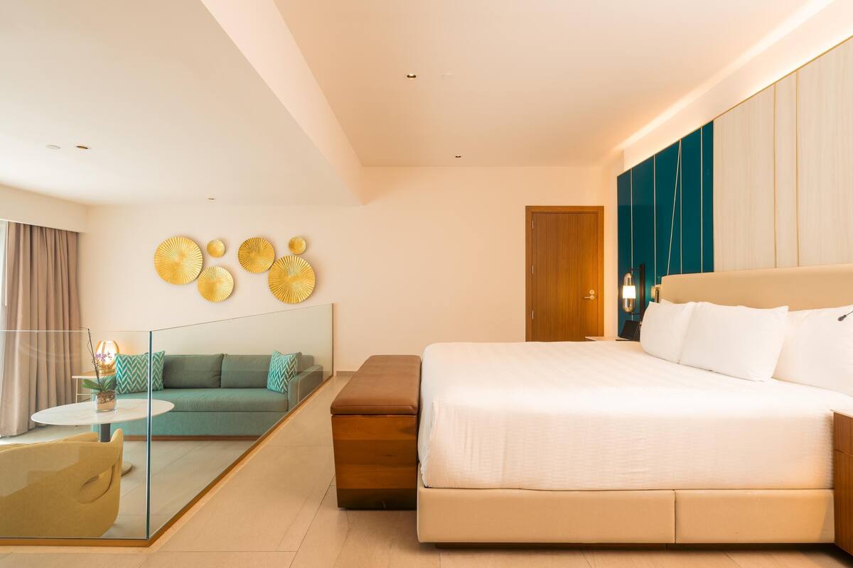 Ein modernes Hotelzimmer mit einem großen Bett, einer Sitzecke, einer Glastrennwand und einer Wanddekoration.