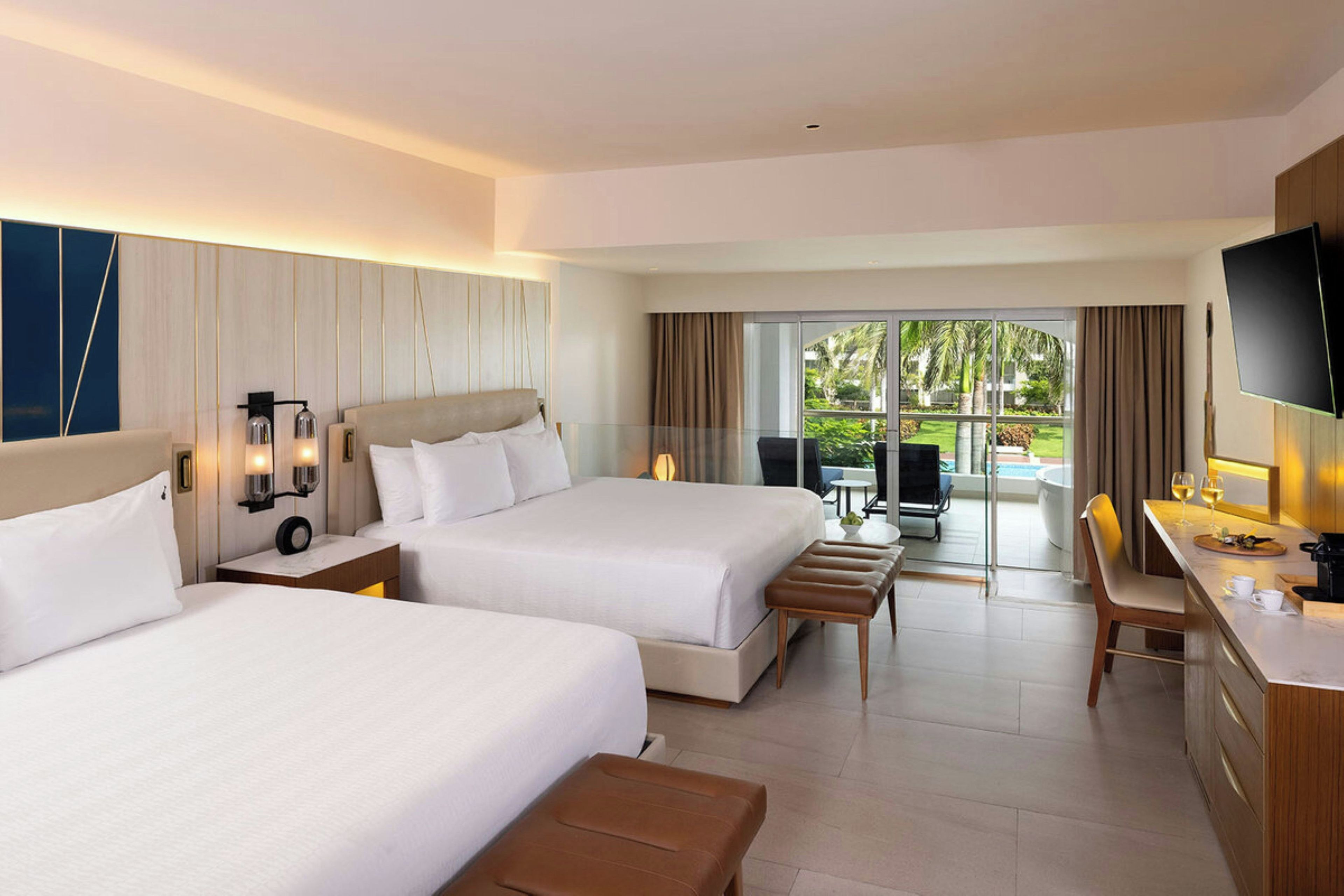 A hotel room with two beds, a desk, a TV, and a view of the outdoors.