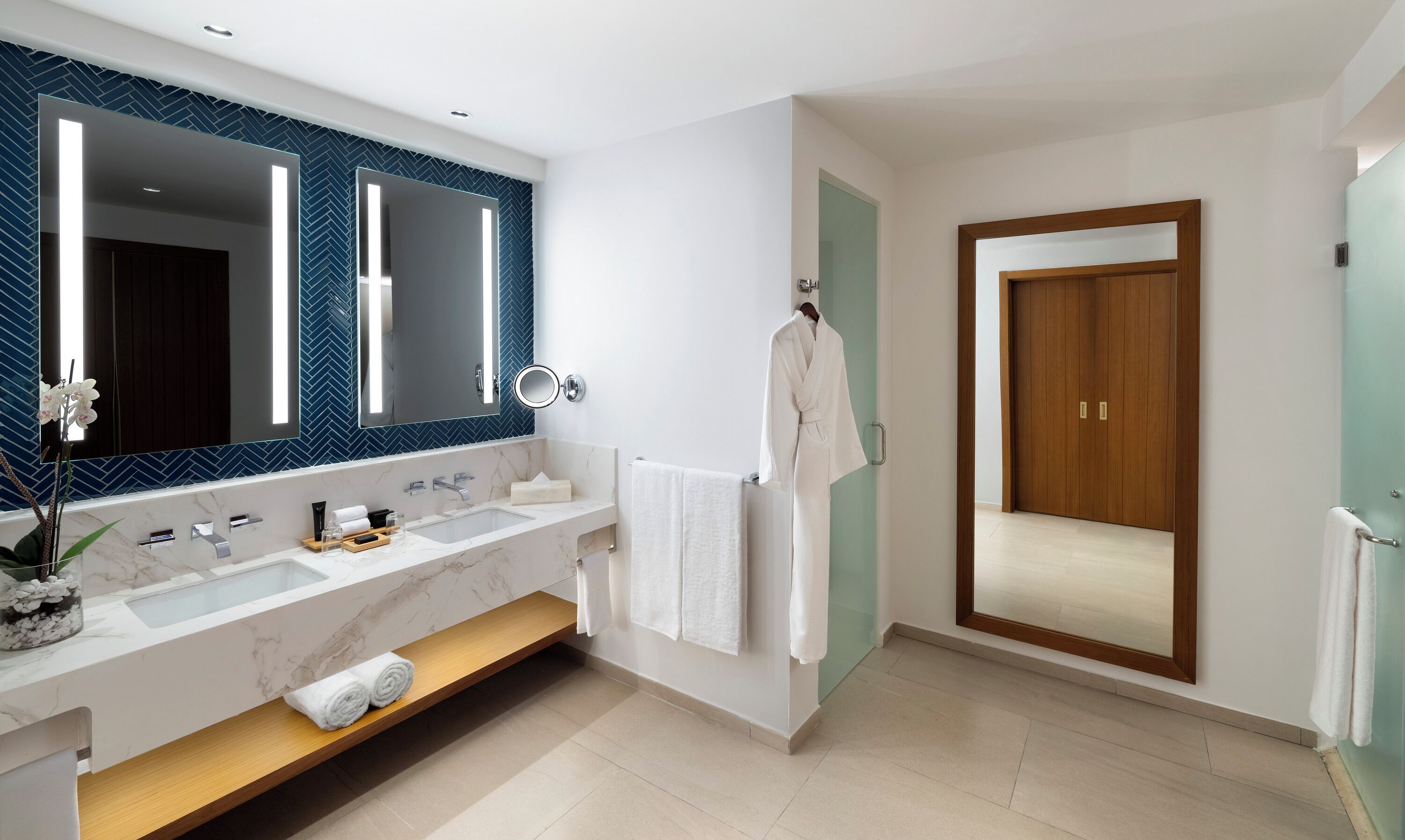 Une salle de bain moderne avec un grand miroir, deux lavabos, un meuble-lavabo et une porte en bois.