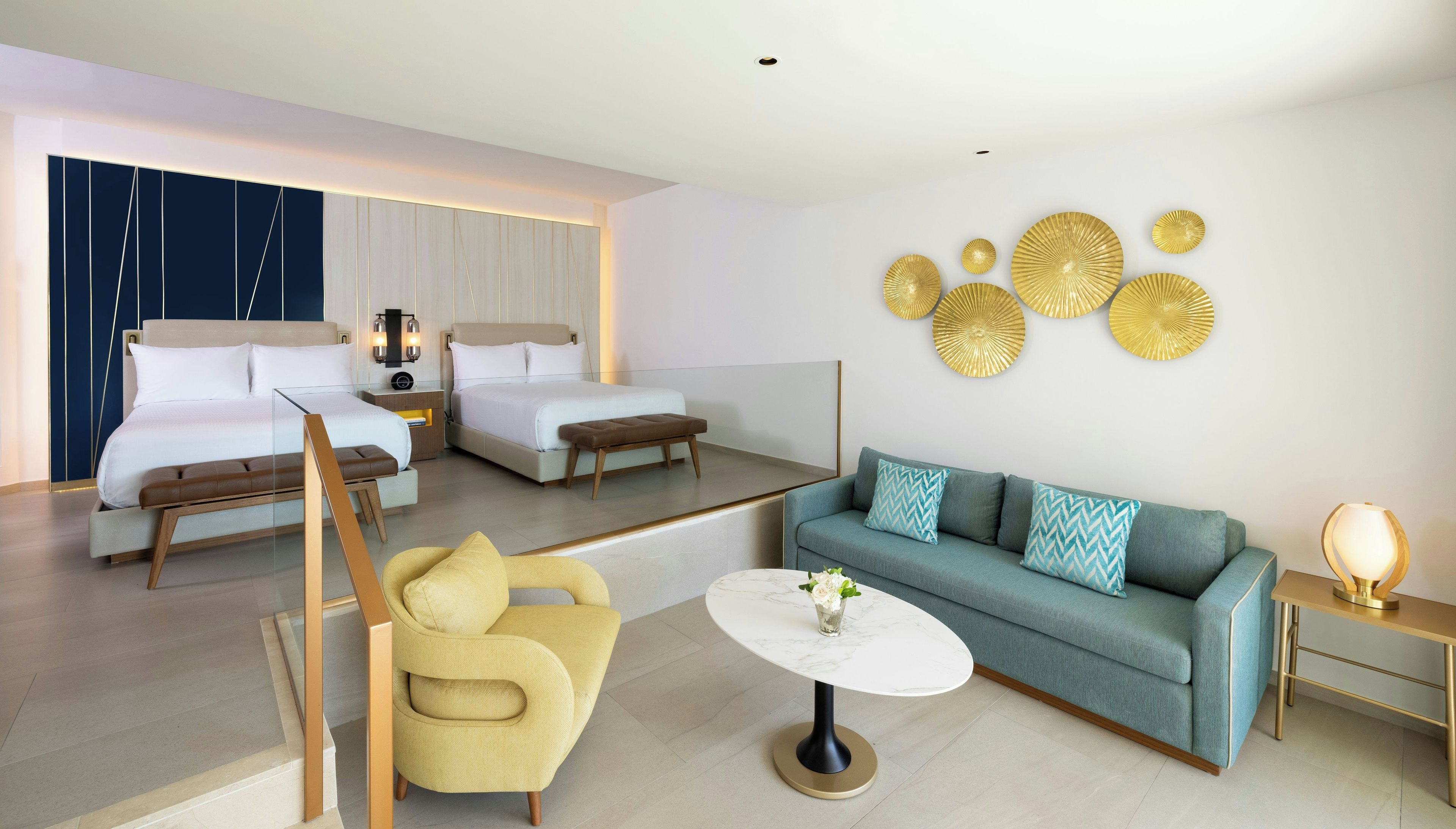 A modern hotel room with a sofa, armchair, and two beds.