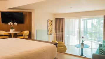 Habitación de hotel con una cama grande, un televisor en la pared, una mesa de comedor con sillas y un balcón con vistas.