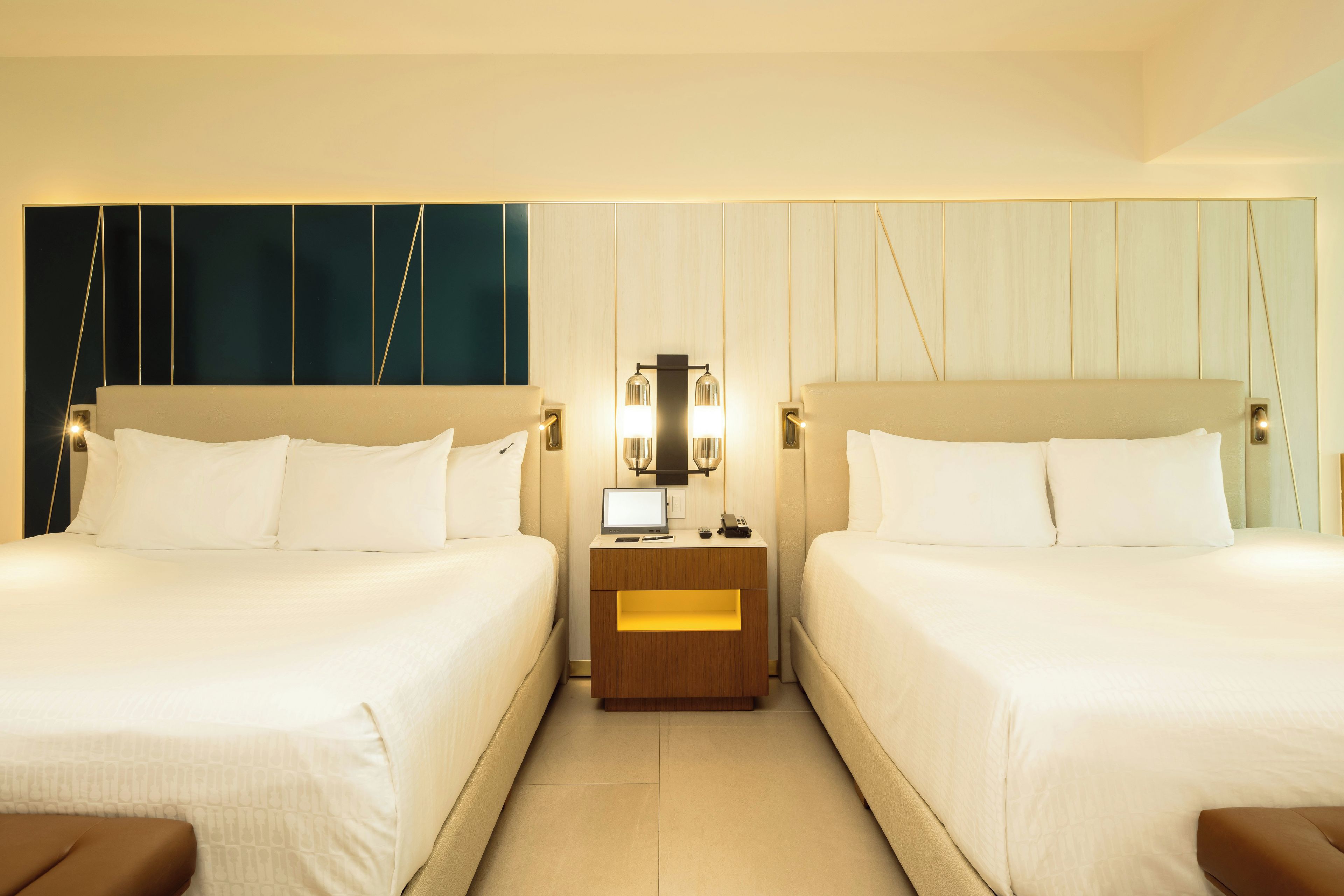 Habitación de hotel con dos camas, una mesita de noche con lámpara y un televisor instalado en la pared.