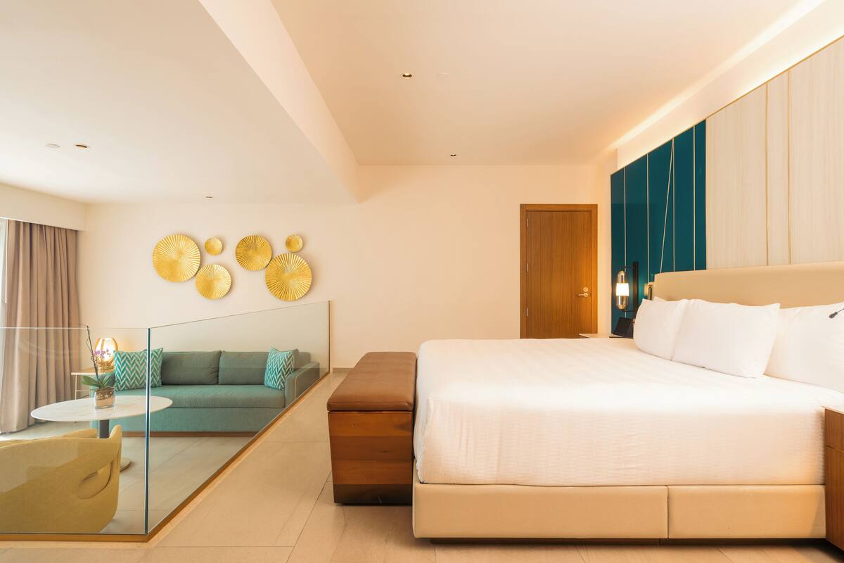 Ein modernes Hotelzimmer mit einem großen Bett, einer Sitzecke, einer Glastrennwand und einem kleinen Tisch mit einer Pflanze.