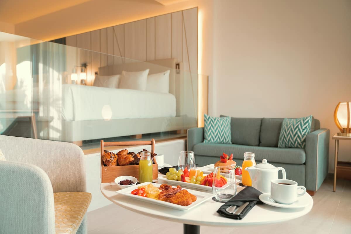 Ein modernes Hotelzimmer mit einem Frühstückstisch, auf dem Gebäck, Früchte und Getränke bereitstehen.