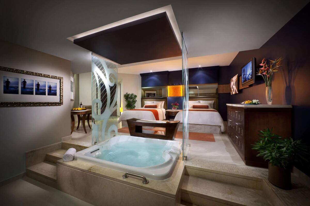Ein modernes Hotelzimmer mit Whirlpool, einem Bett, einem Schreibtisch und einem Badezimmer.