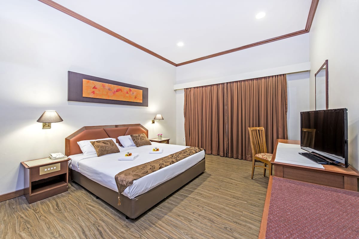 Une chambre d’hôtel avec un grand lit, des tables de chevet, un bureau avec une télévision et une fenêtre avec des rideaux.