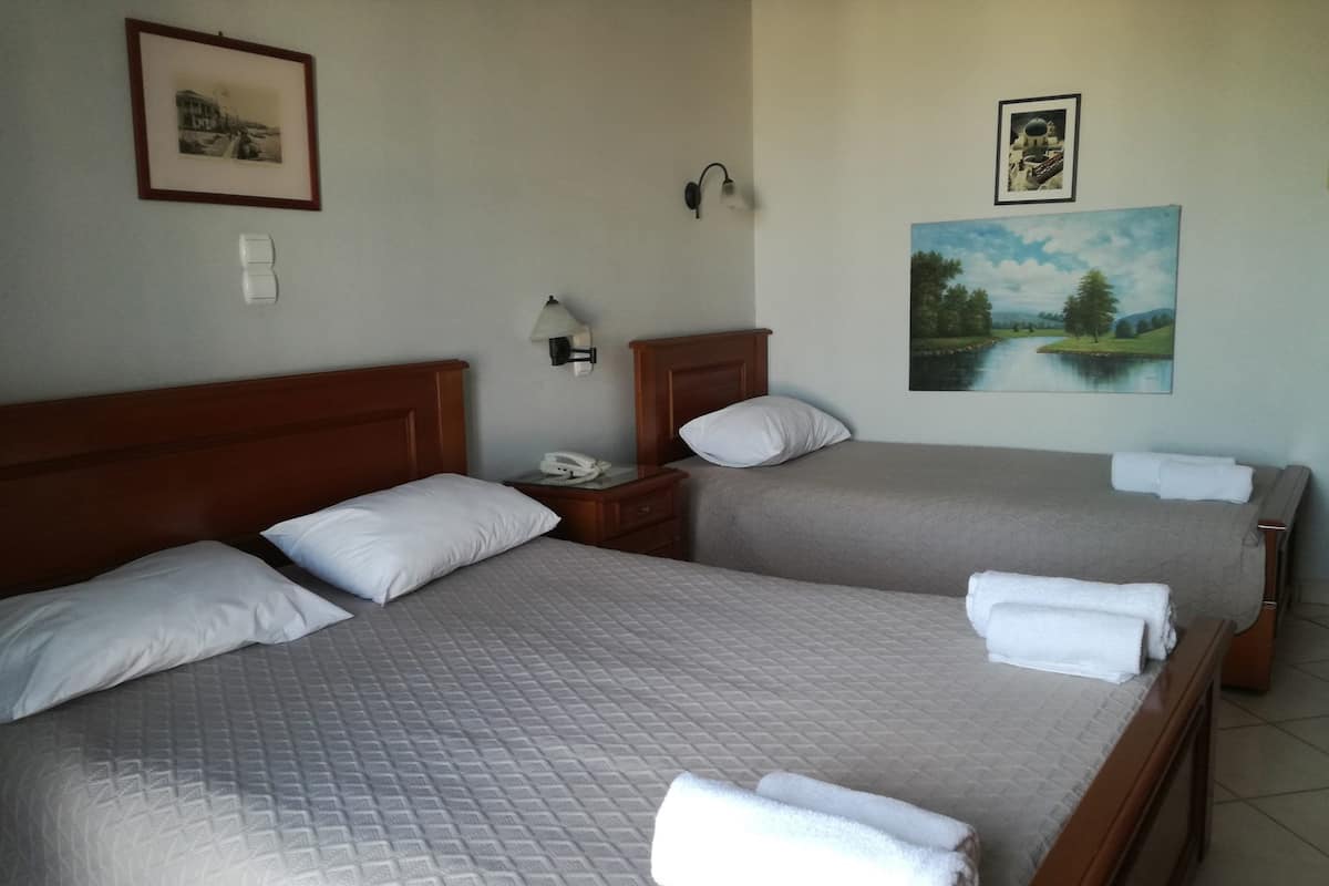 A hotel room with two beds, each with a wooden headboard, white bedding, and a painting of a landscape on the wall.