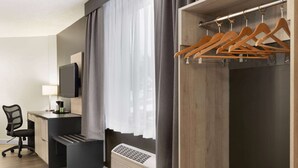A modern hotel room with a desk, chair, TV, and a coat rack. - Travelodge by Wyndham Alma (Alma)