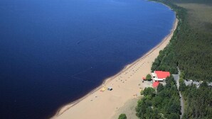 An aerial view of a beach with a red-roofed building, a sandy beach, and a forested area. - Travelodge by Wyndham Alma (Alma)