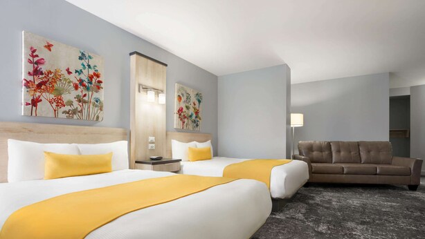 A hotel room with two beds, a sofa, and artwork on the walls. - Travelodge by Wyndham Alma (Alma)