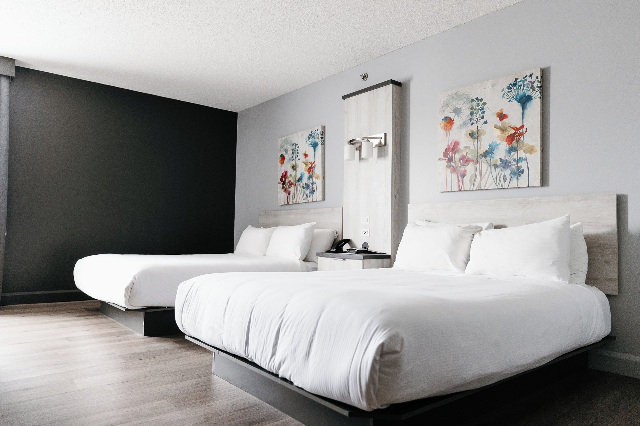 A hotel room with two beds, a dark accent wall, and floral artwork.