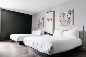Une chambre d’hôtel avec deux lits, un mur d’accent de couleur sombre et des œuvres d’art florales.
