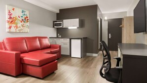 A modern living room with a red sofa, a kitchen area with white cabinets, and a dining area with a black chair. - Travelodge by Wyndham Alma (Alma)