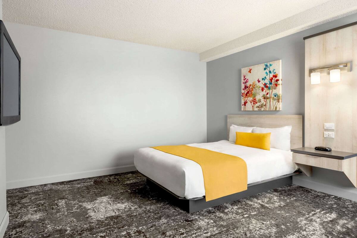 Ein Hotelzimmer mit Bett, Nachttisch, einem Gemälde und einer Wandleuchte.