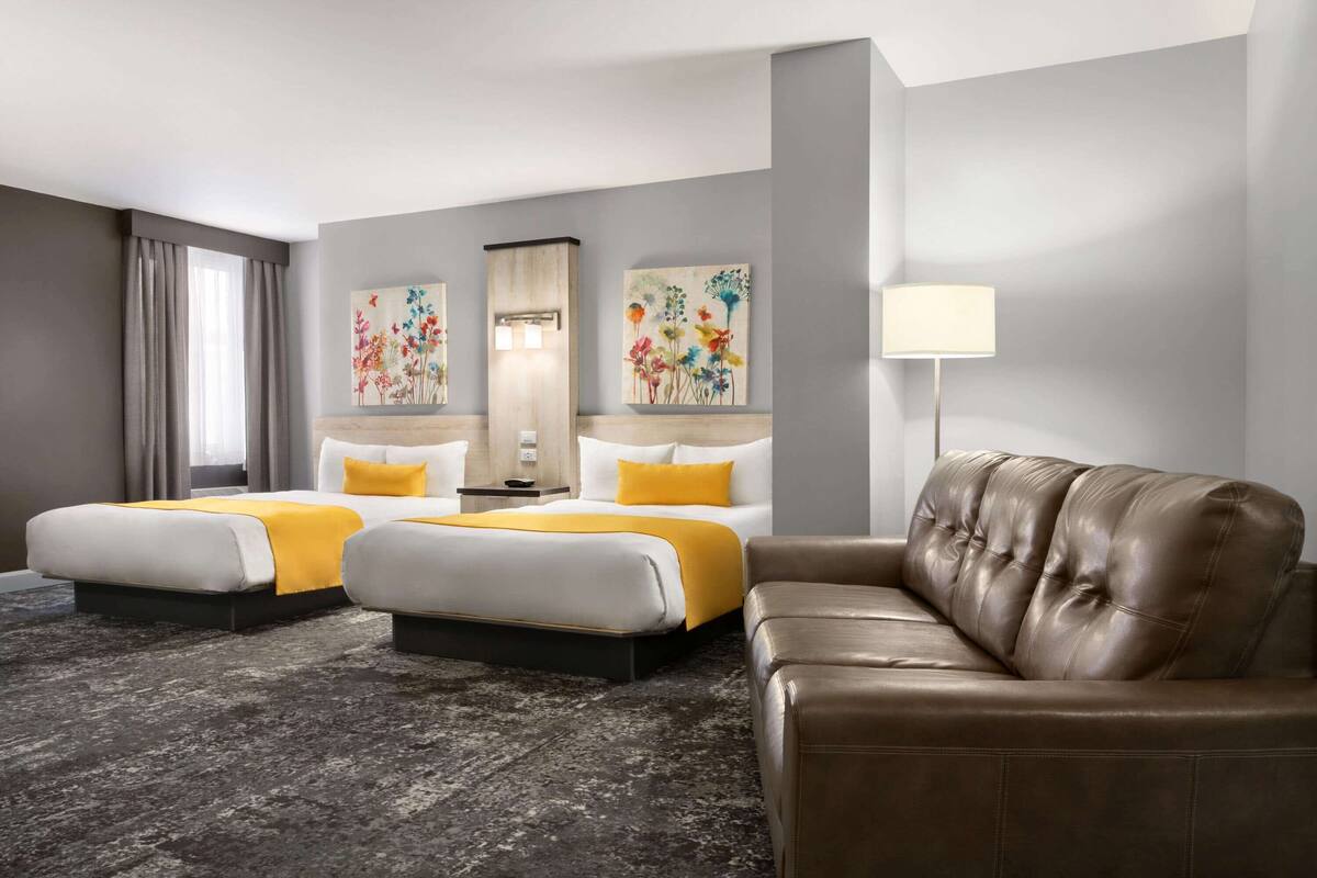 Ein Hotelzimmer mit zwei Betten, einem braunen Ledersofa und floralen Bildern an den Wänden.