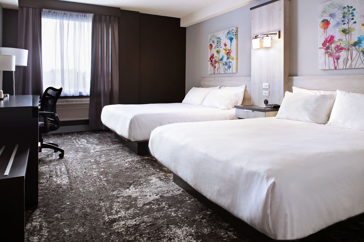 Ett hotellrum med två sängar, ett skrivbord, en stol och konstverk på väggarna.