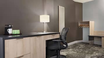 Une chambre d’hôtel équipée d’un bureau, d’une chaise, d’une lampe, d’une machine à café et d’un porte-manteau.