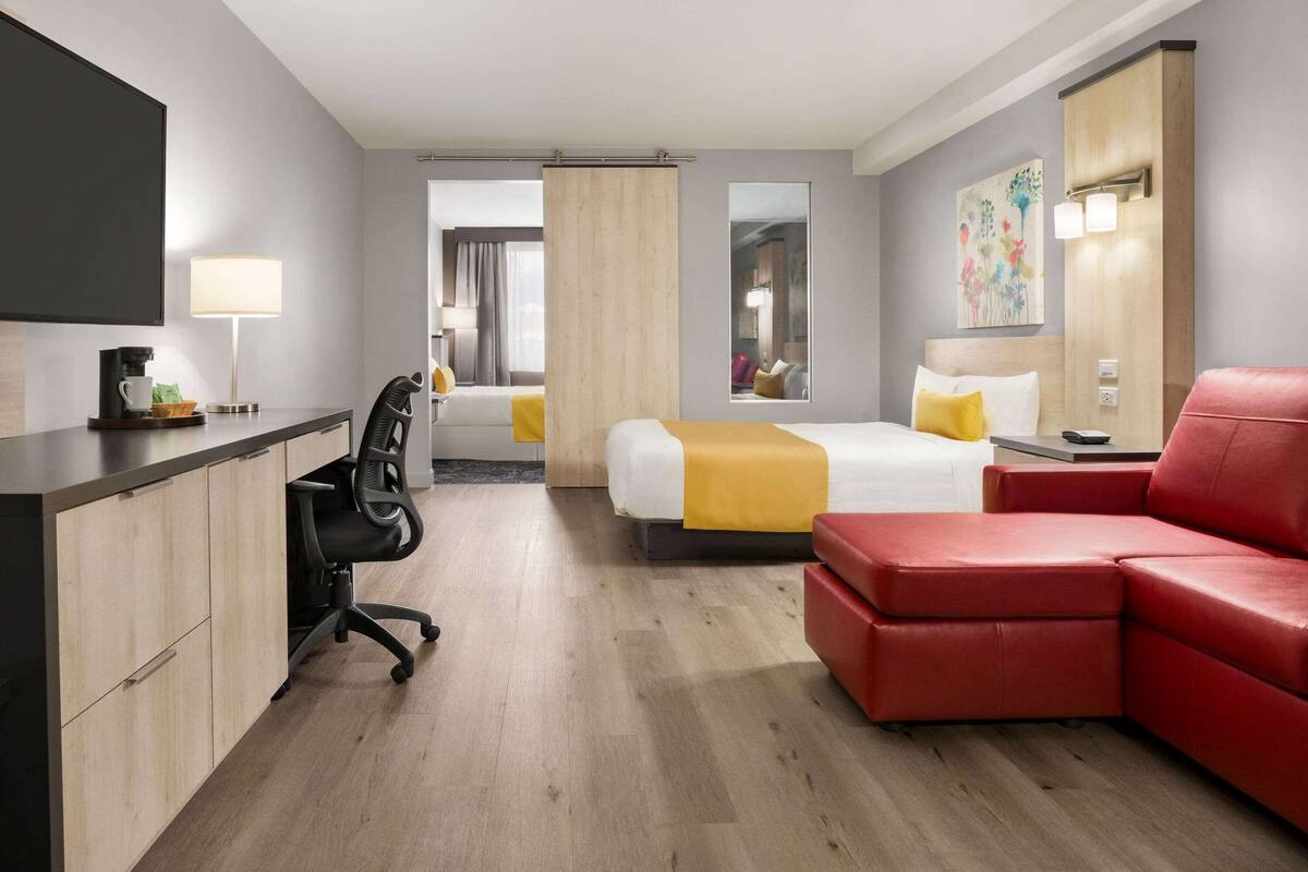 Ein Hotelzimmer mit Schreibtisch, Stuhl, Bett mit gelber Decke, rotem Sofa und großem Spiegel.