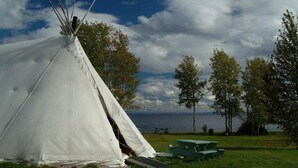 A white teepee with a picnic table and benches nearby, set against a backdrop of trees and a body of water. - Travelodge by Wyndham Alma (Alma)