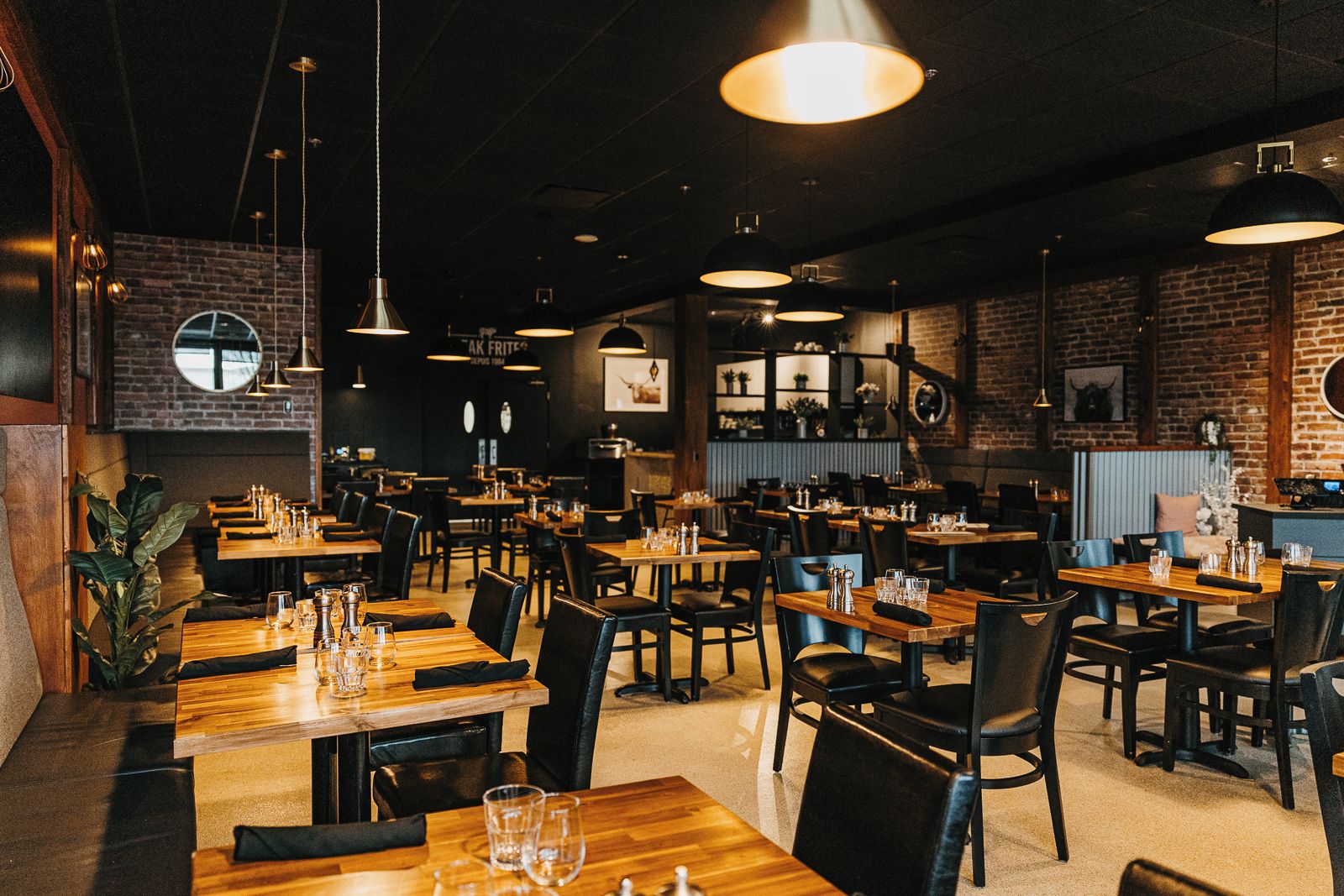 A restaurant interior with multiple tables and chairs, hanging pendant lights, and brick walls.