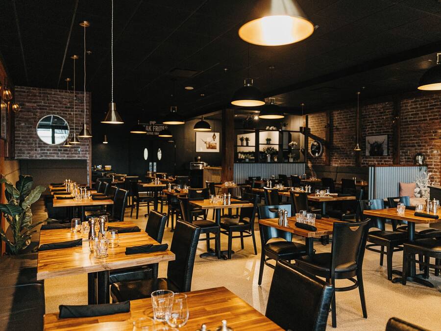 Interior de restaurante con varias mesas y sillas, lámparas colgantes y paredes de ladrillo.
