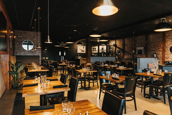 L’intérieur d’un restaurant avec de nombreuses tables et chaises, des luminaires suspendus et des murs en briques.