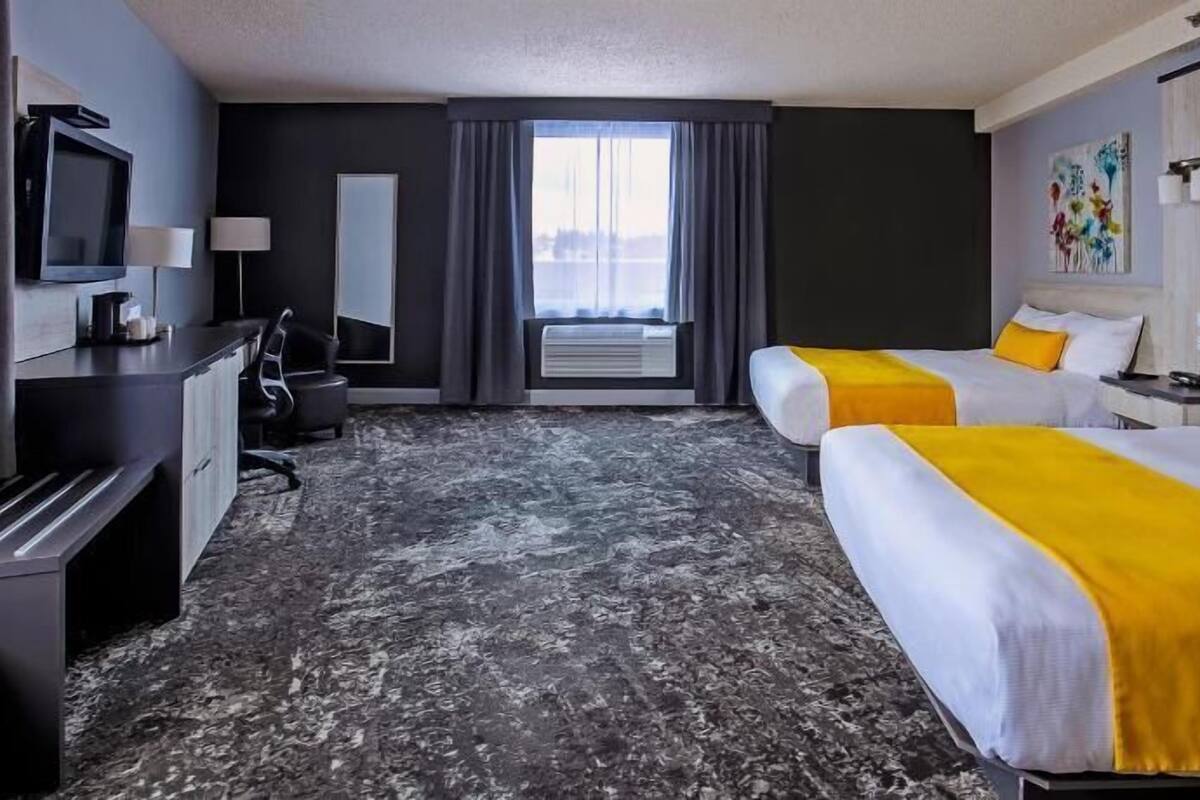 Ein Hotelzimmer mit zwei Betten, einem Schreibtisch, einem Fernseher und einem großen Fenster.