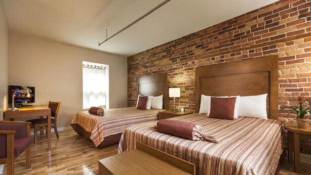 Une chambre d’hôtel avec deux lits, un bureau en bois, une télévision et un mur en briques.