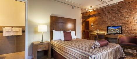 Una habitación de hotel moderna con suelo de madera, una cama grande con ropa de cama a rayas, un televisor y una pared de ladrillo.