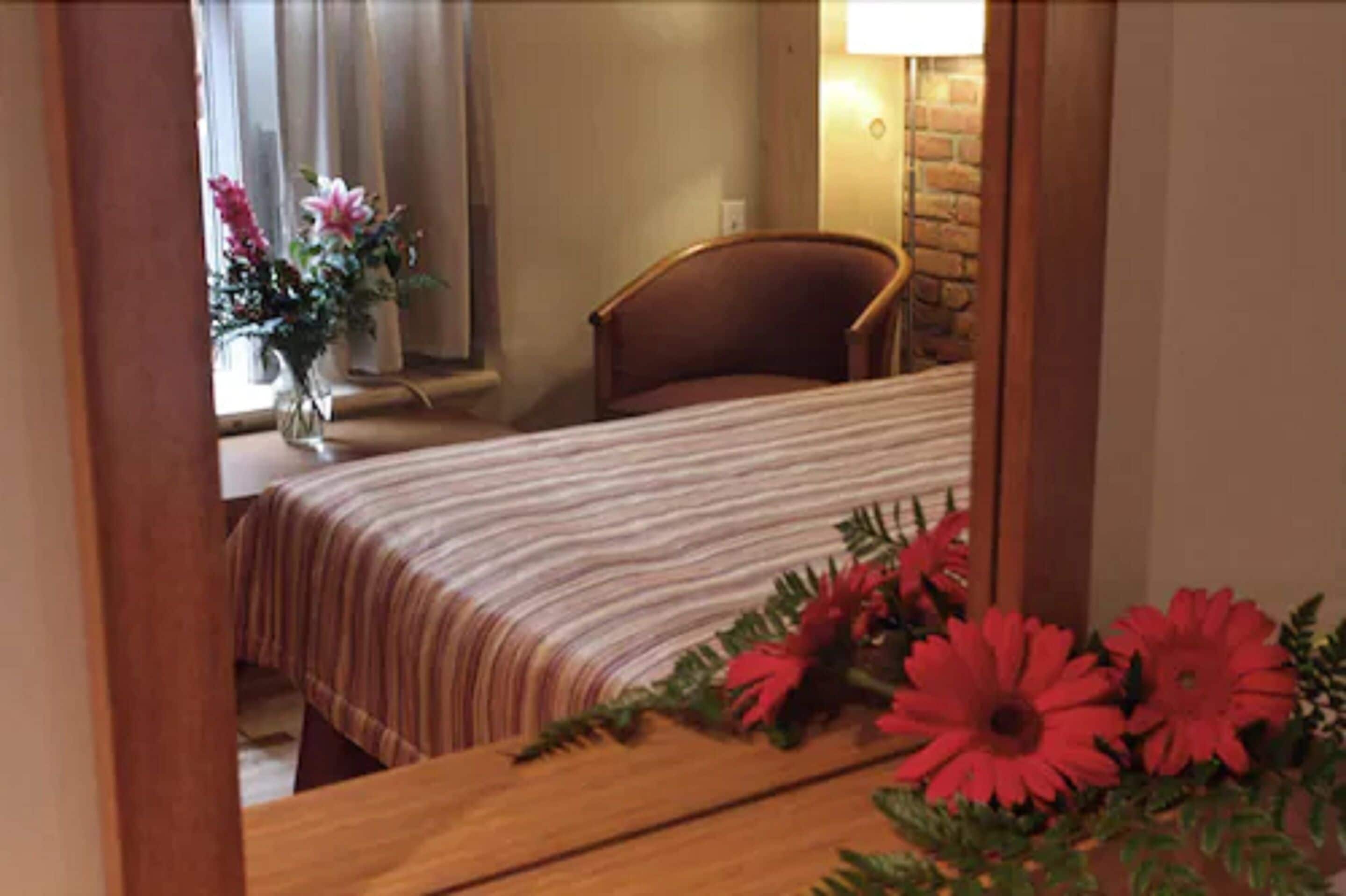 A bedroom with a bed, a chair, a vase with flowers, and a lamp.