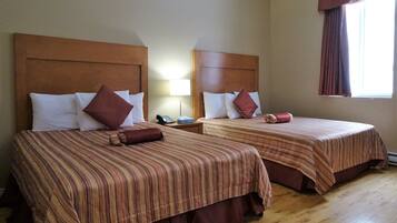 Two double beds with striped bedding, wooden headboards, and a bedside table with a lamp.