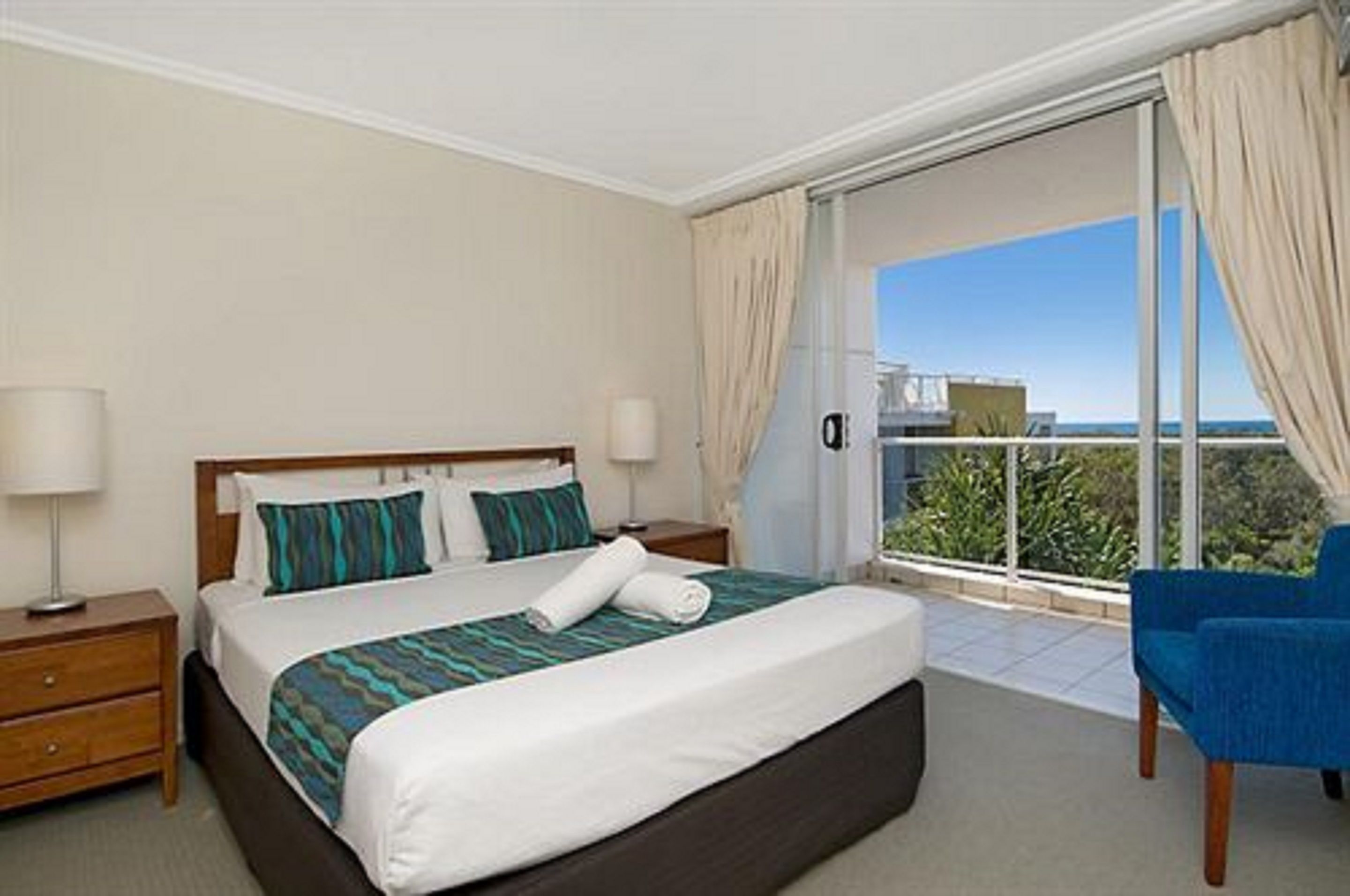 Une chambre d’hôtel avec un lit, une table de chevet, une chaise et un balcon avec vue.