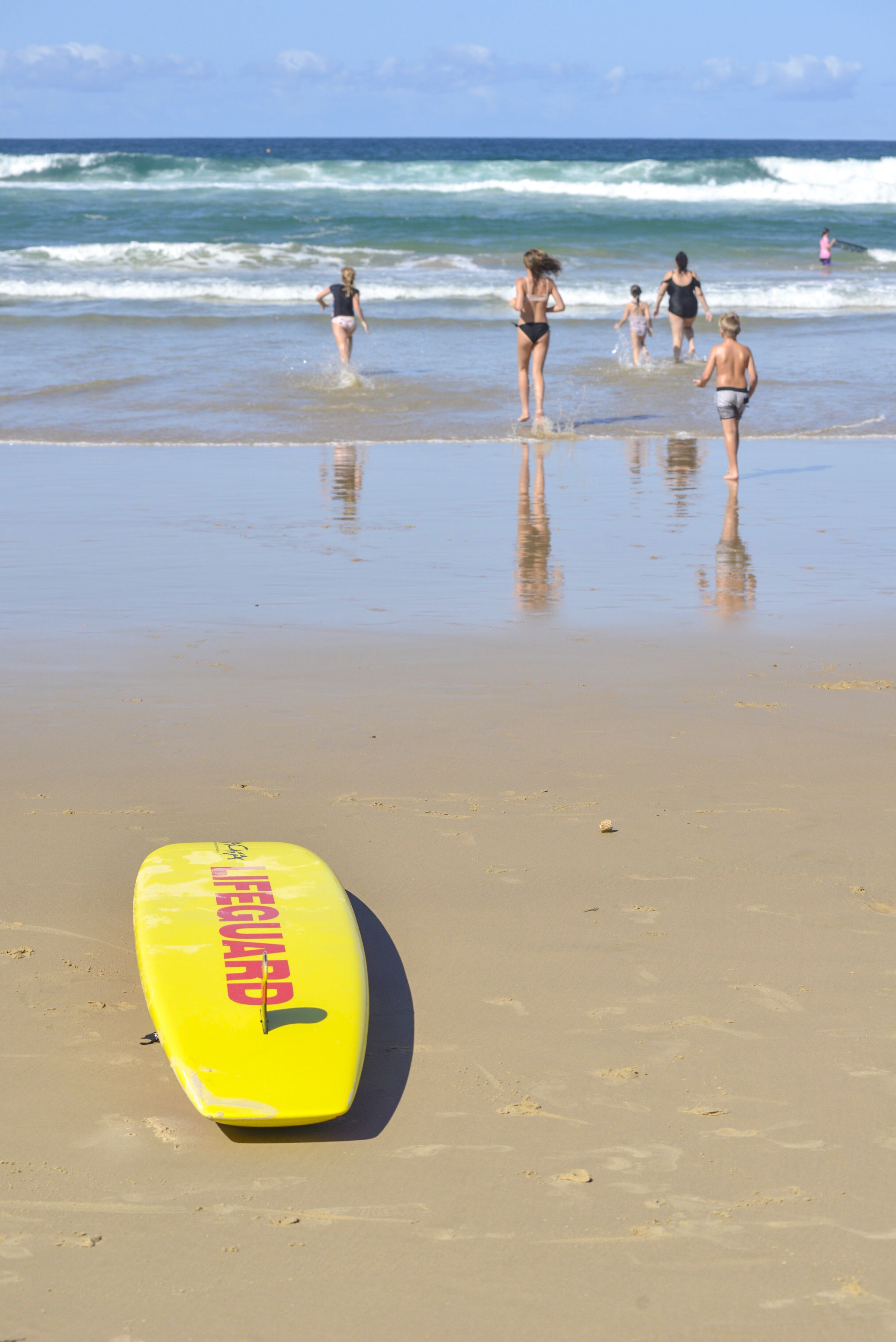 Un poste de surveillance des sauveteurs se dresse sur une plage de sable, avec des personnes dans l’eau et sur le rivage.
