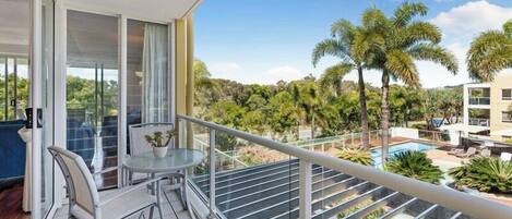 Un balcone con un tavolo e sedie in vetro, con vista su una piscina e palme.
