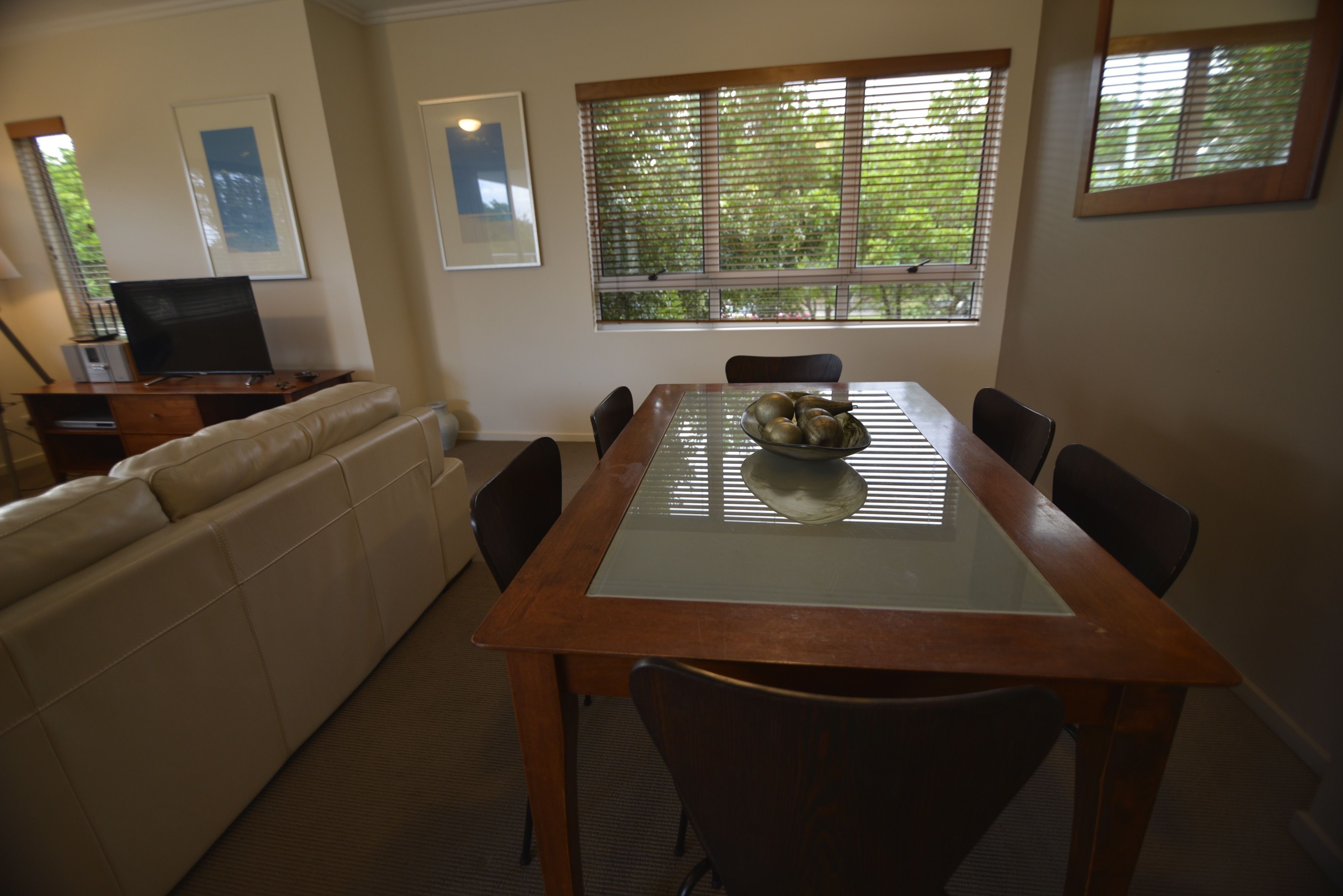 Un área de comedor con una mesa de vidrio, seis sillas, un banco de madera, un sofá y una ventana con persianas.