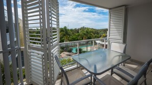 Un balcon doté d’une table et de chaises en verre, offrant une vue sur une piscine et une végétation luxuriante.