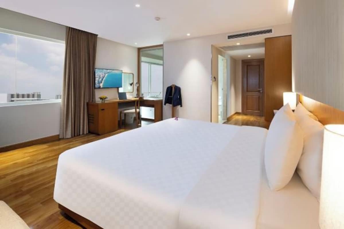 A hotel room with a large bed, a desk with a chair, a television, and a view of the city.