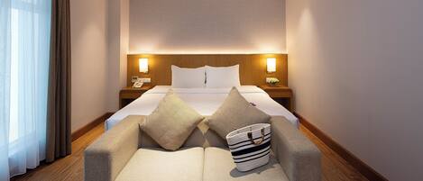 Habitación de hotel con cama, mesitas de noche, sofá y suelo de madera.