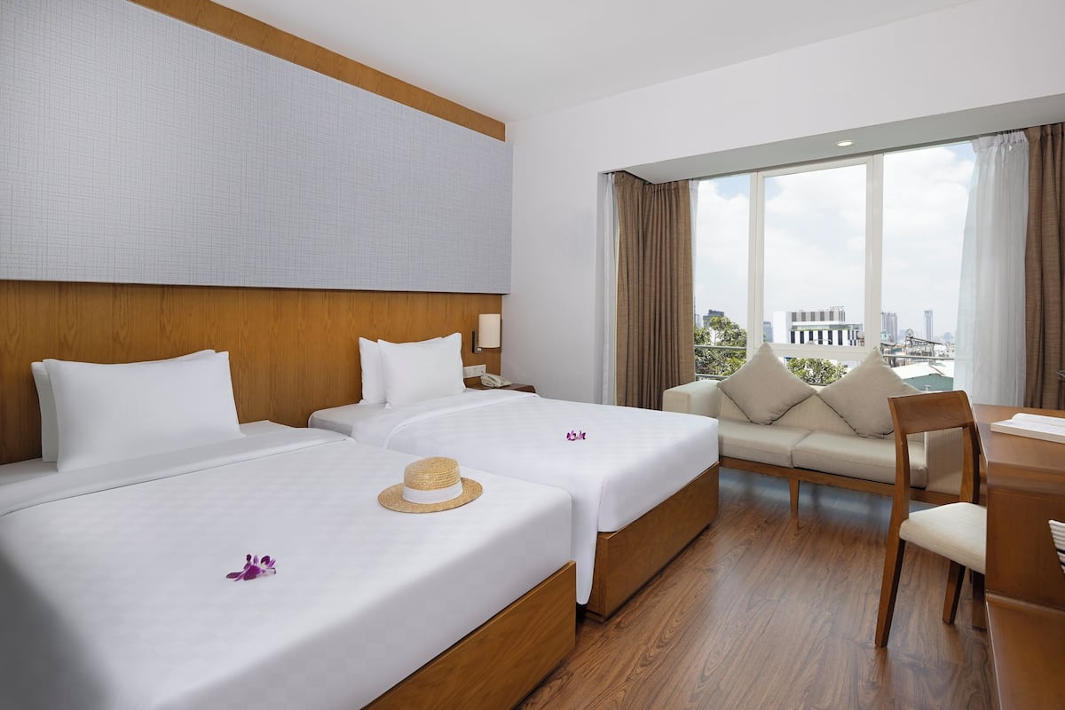 Quarto de hotel com duas camas, um sofá, uma mesa de jantar e vista para a cidade.