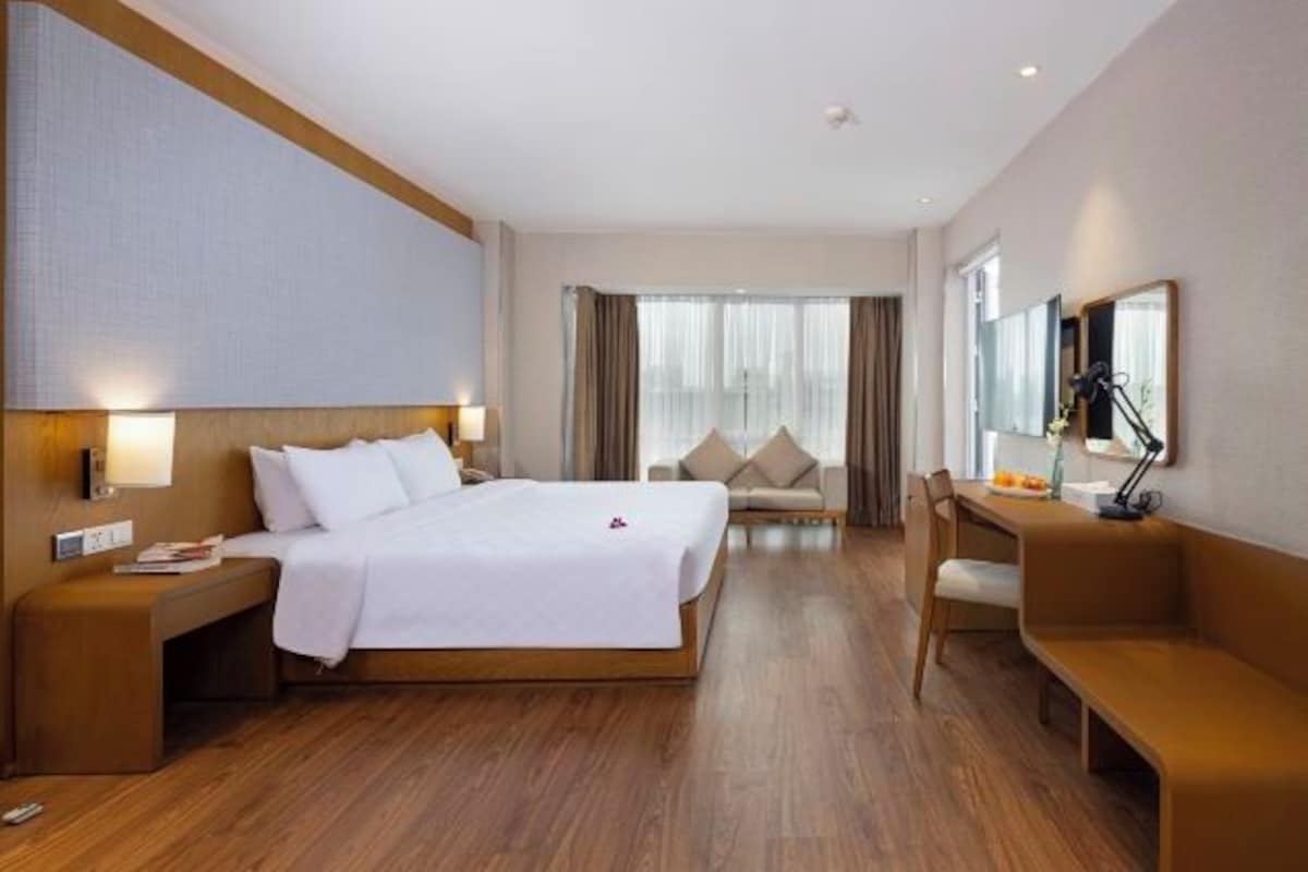 A hotel room with a large bed, a desk, a chair, and a sofa.