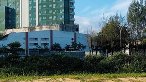 Een meerhoog gebouw met een plat dak, omringd door groen en een zandig gebied.