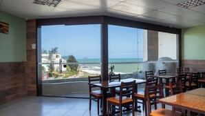 Een restaurant met grote ramen met uitzicht op de oceaan en een strand.