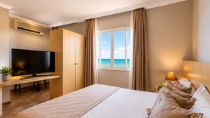 Een hotelkamer met een bed, een televisie, een bureau en een raam met uitzicht op zee.
