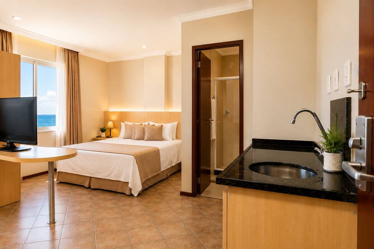 A hotel room with a bed, desk, TV, and a view of the sea.