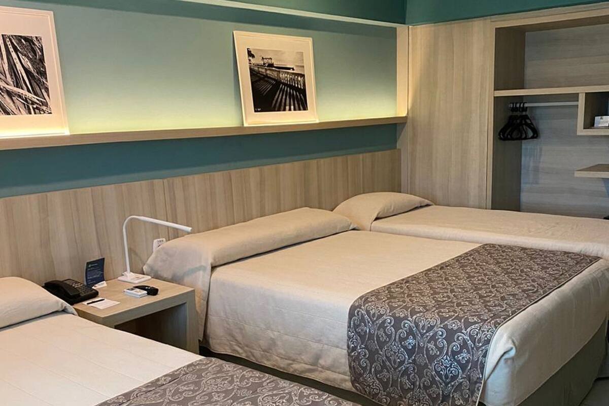 Ein Hotelzimmer mit zwei Betten, einem Nachttisch mit Telefon und einem kleinen Tisch. An der Wand hängen Bilder in Rahmen, und es gibt einen Schrank mit Spiegel.