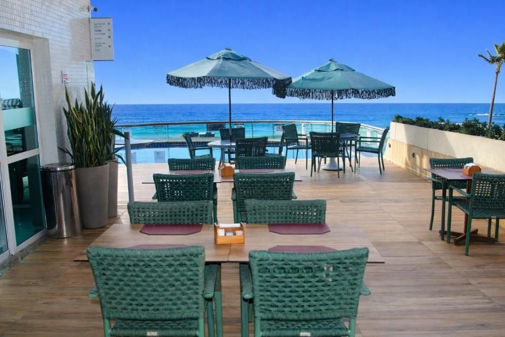 A rooftop bar with a pool view, green wicker furniture, and umbrellas.