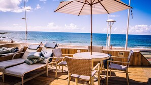 Een terras met rieten meubilair, een ronde tafel en een gestreepte parasol met uitzicht op de oceaan.