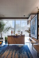 Un moderno vestíbulo de hotel con un mostrador de recepción de madera, ventanas amplias y una alfombra azul estampada.